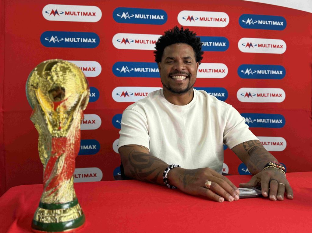 A smiling man posing with the FIFA World Cup trophy in front of a Multimax backdrop.