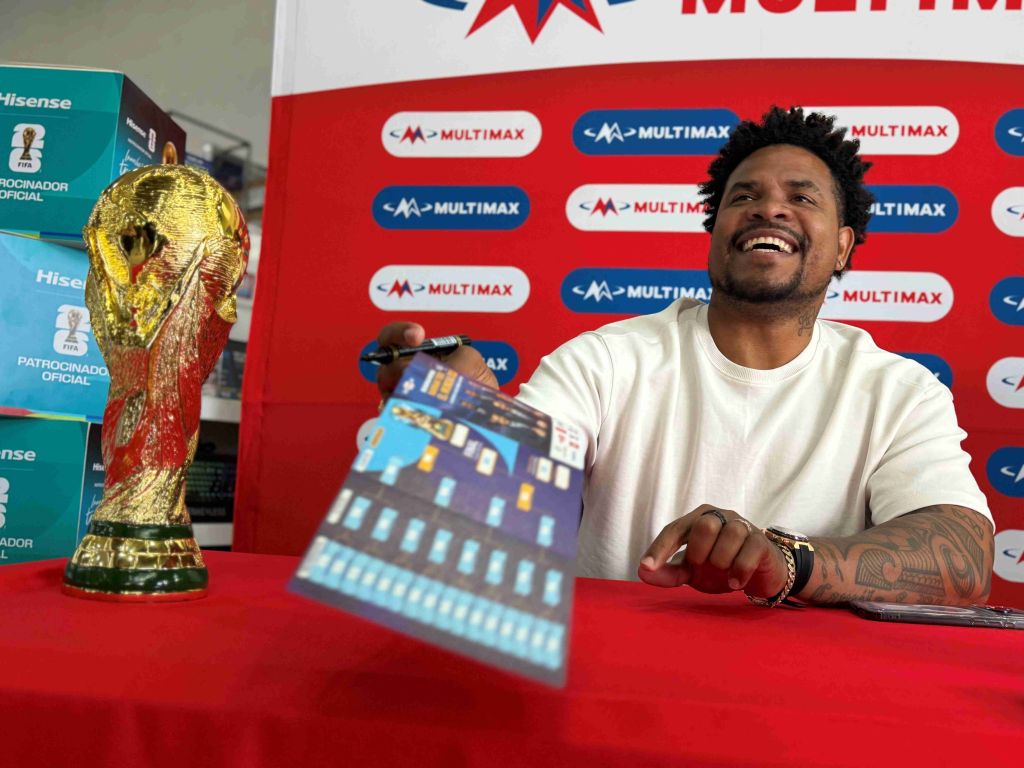 A smiling man holding a soccer trophy in front of a Multimax branded backdrop.