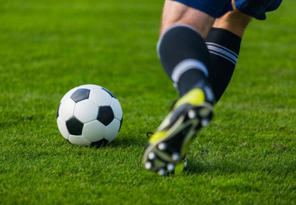 A soccer ball on a grassy field, with a player's foot about to kick it.