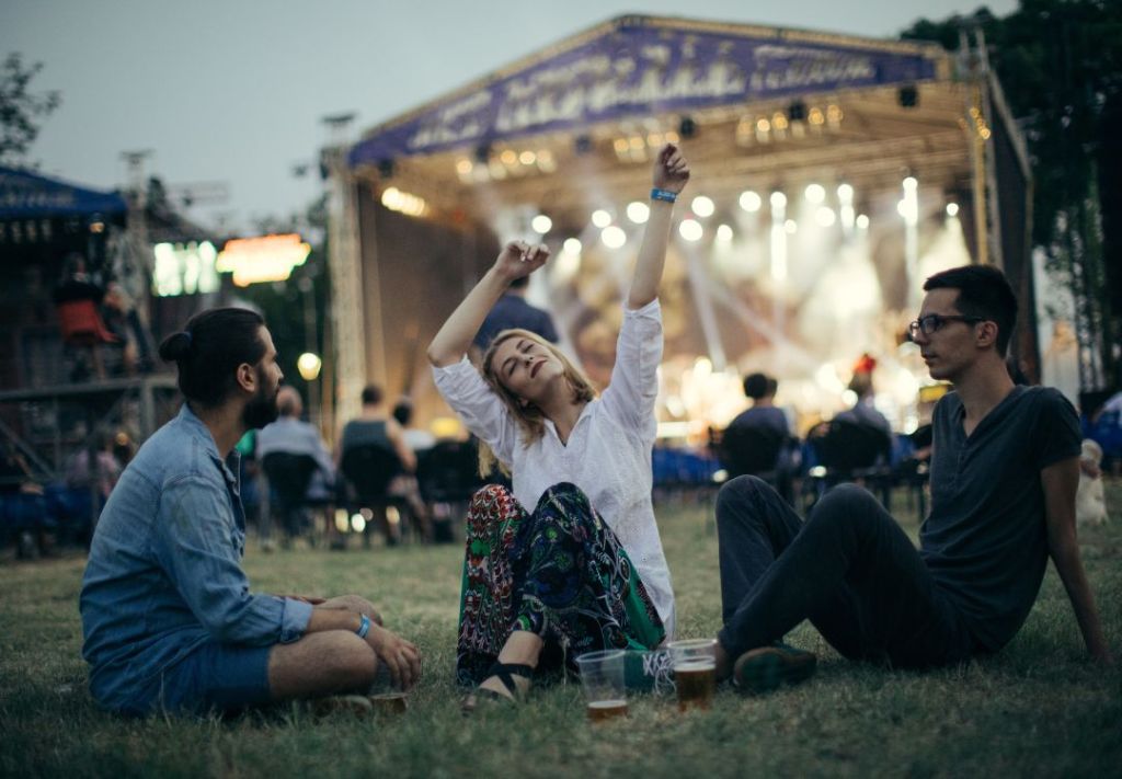 A group of people enjoying a music festival, with a woman dancing and raising her arms in the foreground.