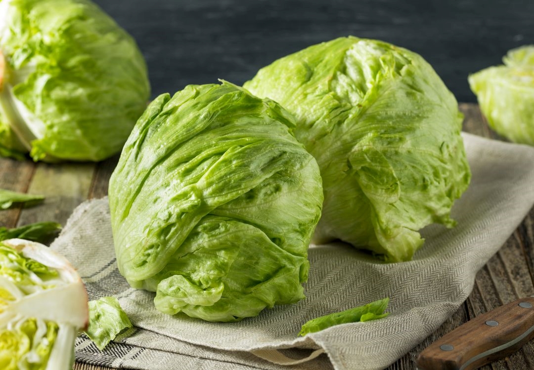 Several fresh green lettuce heads on a gray cloth on a wooden surface.