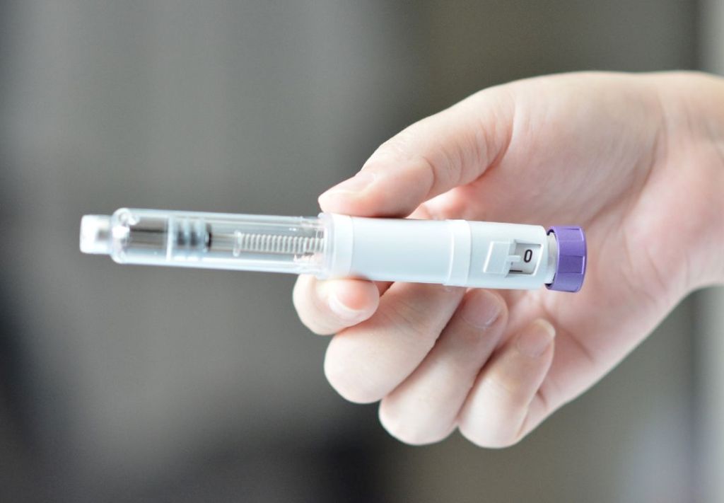 A hand holding a syringe with a clear liquid and a purple cap.