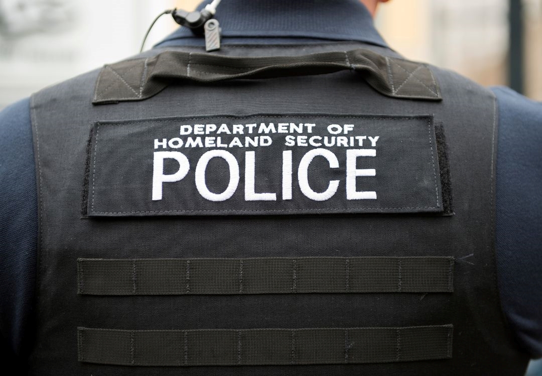 A person wearing a black jacket with "DEPARTMENT OF HOMELAND SECURITY POLICE" printed on the back.