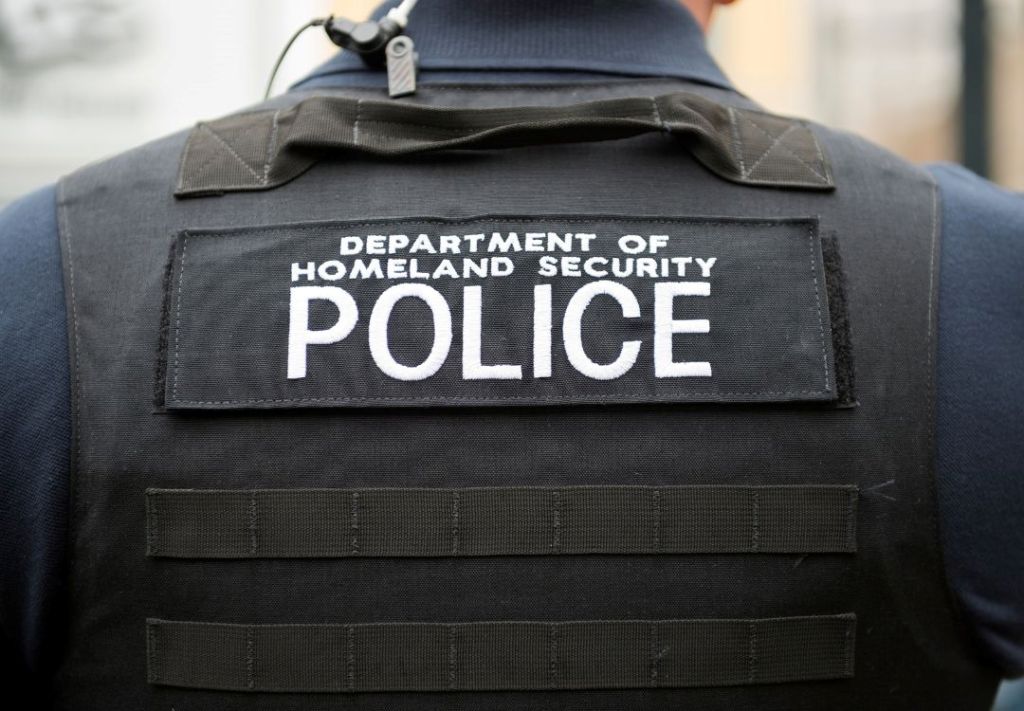 A person wearing a black jacket with "DEPARTMENT OF HOMELAND SECURITY POLICE" printed on the back.