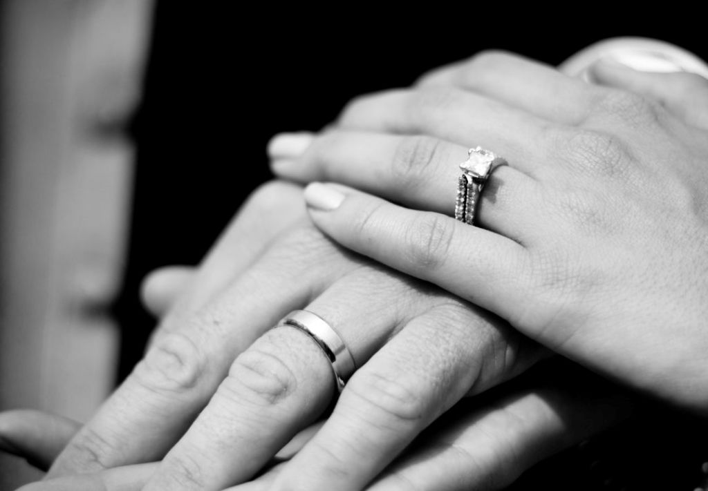 Hands clasped together, wearing wedding rings, in a black and white image.