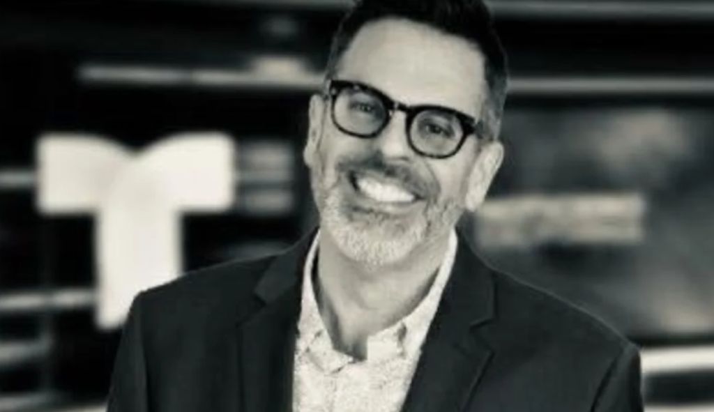 A smiling man with glasses and a beard wearing a black suit jacket.