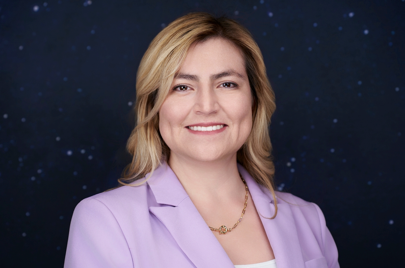 Smiling woman with blonde hair wearing a lavender blazer against a starry night sky background.