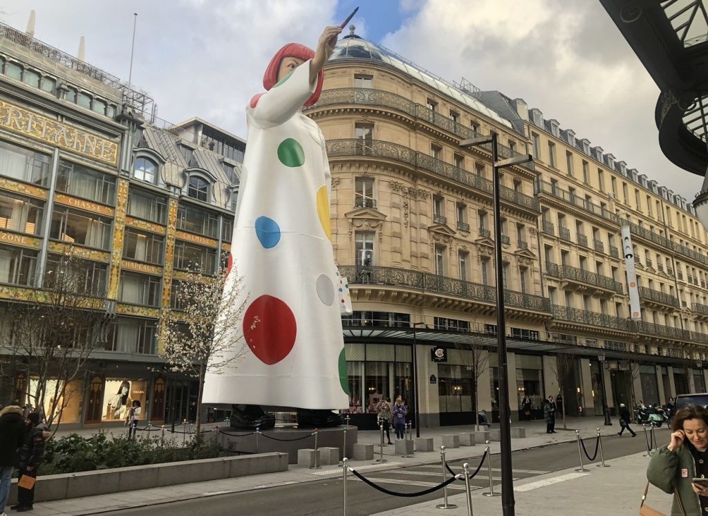 A large white sculpture with colorful polka dots stands in front of a historic Parisian building with ornate architecture.